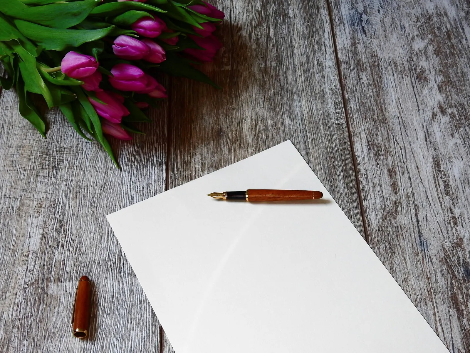 A blank note with a fountain pen and purple tulips on a wooden table, ideal for personalized messages.